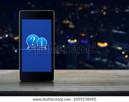 Question mark and information chat icon on modern smart mobile phone screen on wooden table over blur colorful night light city tower and skyscraper, Business customer service and support online