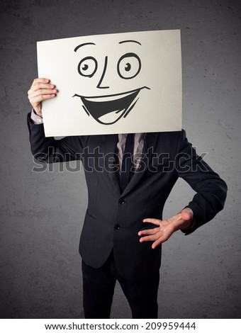 Young businessman holding a cardboard with a smiley face on it in front of his head