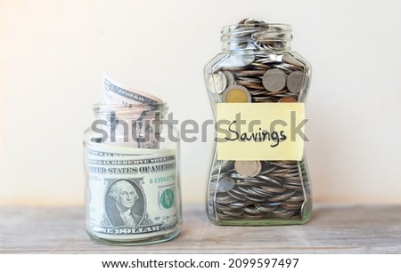 Coins and dollars savings in glass jar filled isolated on vintage wooden table.