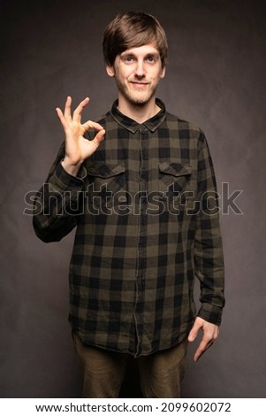 Young handsome tall slim white man with brown hair making okay sign with flannel shirt on grey background