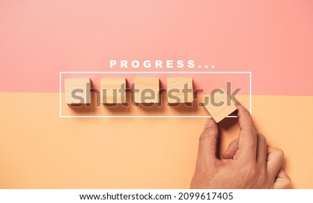 Hand putting wooden cube block on half of pink and orange background with graphic loading for project job progressive concept. Royalty-Free Stock Photo #2099617405