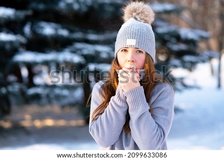 freezing woman, a young beautiful frozen girl in the snow suffers from cold icy weather, shakes, trembles outside on an icy snowy day, low temperature, breathes with her hands, tries to keep warm Royalty-Free Stock Photo #2099633086