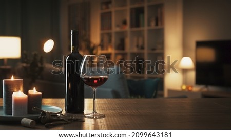 Red wine tasting at home: wine bottle, wineglass, corkscrew and candles on a table in the living room at night Royalty-Free Stock Photo #2099643181