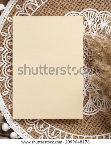 Blank paper card on bohemian jute placemat near pampas grass top view. Boho rustic scene with greeting or Invitation vertical card mockup, flat lay. 