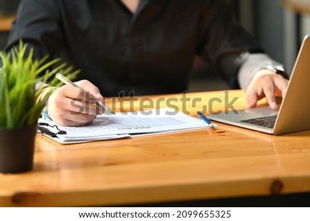 Cropped image of a businessman writing on a paperwork at the wooden table.