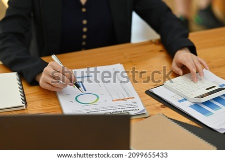 Cropped image of a young accountant woman calculates the business growth at the wooden table surrounded by a computer laptop and business paperwork.