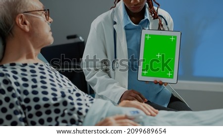 Surgeon woman holding green screen tablet in hospital ward to show sick patient examination test results for starting healing treatment. African american specialist giving health advice