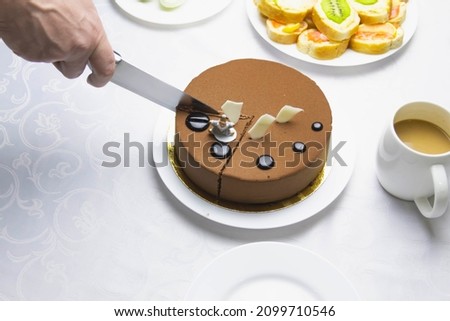 On the festive table with a white tablecloth there is a chocolate cake, which is cut with a knife by a man.