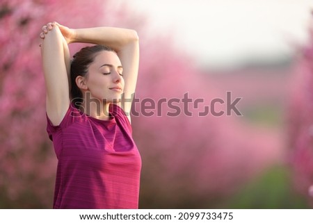 Sportswoman stretching arms and relaxing in a field after sport Royalty-Free Stock Photo #2099733475