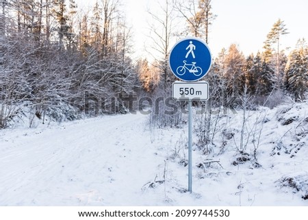 A sign indicates the presence of a pedestrian and bicycle trail after 550 meters. Forest road on a snowy winter day.