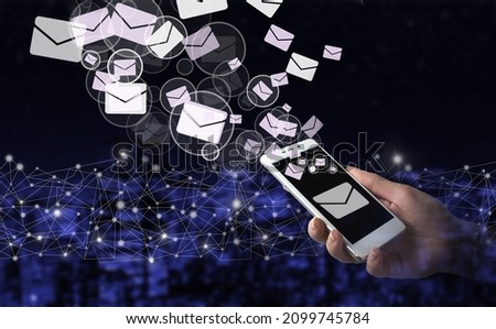 Sending email. Bulk mail. Hand hold white smartphone with digital hologram Email and sms sign on city dark blurred background. Business email concept