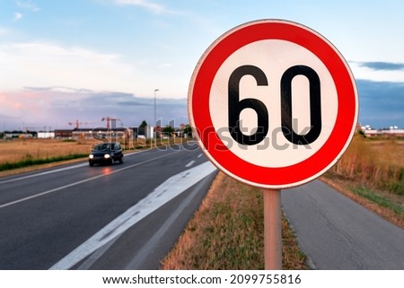 Speed limit at 60 kmph traffic sign by the road, blurred car in motion in background