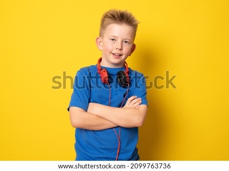 Cute boy wearing headphones standing with arms folded isolated over yellow background.