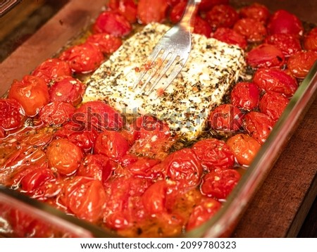 Cherry tomatoes and feta cheese melted in the oven make a delicious dinner. A fork mashes the cheese.
