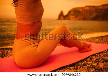 Middle aged well looking woman with black hair, fitness instructor in leggings and tops doing stretching and pilates on yoga mat near the sea. Female fitness yoga routine concept Healthy lifestyle