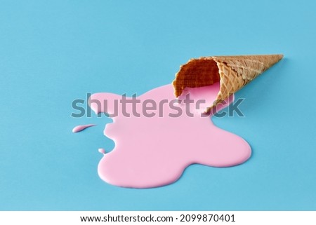 Pink ice cream melting and spilling from the waffle cone on pastel blue background. Minimalistic summer food concept. Royalty-Free Stock Photo #2099870401