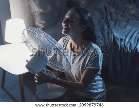 Woman in her bedroom on a hot summer night, she is enjoying fresh air in front of a fan Royalty-Free Stock Photo #2099879746