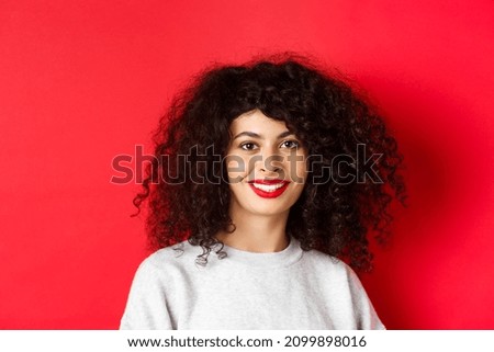 Close-up of beautiful lady with red lips and curly hair, smiling and looking happy at camera, studio background