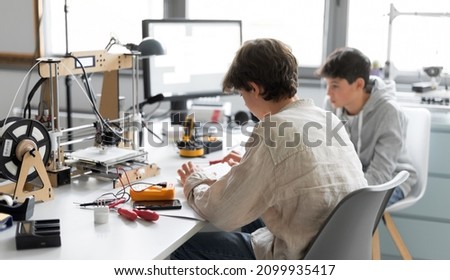 Students sitting at desk in the lab and learning 3D printing together, one is typing and the other is assisting him Royalty-Free Stock Photo #2099935417