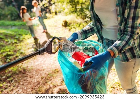 Volunteers cleaning up the park, a woman is putting trash in a garbage bag and some kids are helping her, environmental protection concept Royalty-Free Stock Photo #2099935423