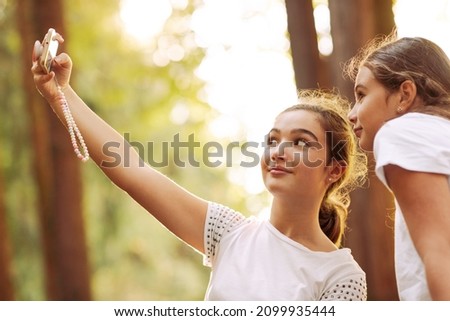 Cute young girls posing together in the forest, they are taking selfies with a smartphone