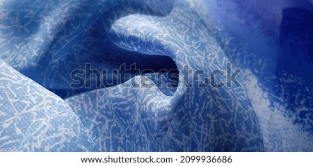 Wavy blue fabric with white abstract print, in folds (macro, texture).
