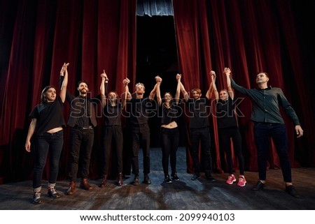 People bowing to audience. Group of actors in dark colored clothes on rehearsal in the theater. Royalty-Free Stock Photo #2099940103
