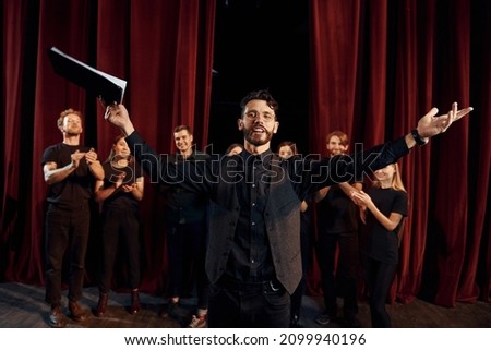 Man is practicing his role. Group of actors in dark colored clothes on rehearsal in the theater. Royalty-Free Stock Photo #2099940196