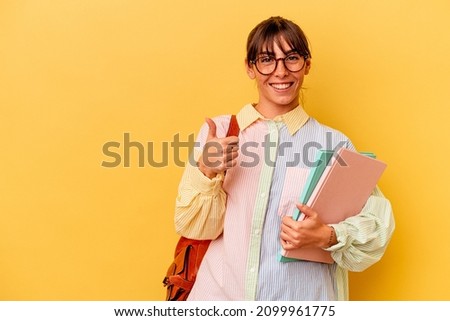 Young student Argentinian woman isolated on yellow background smiling and raising thumb up