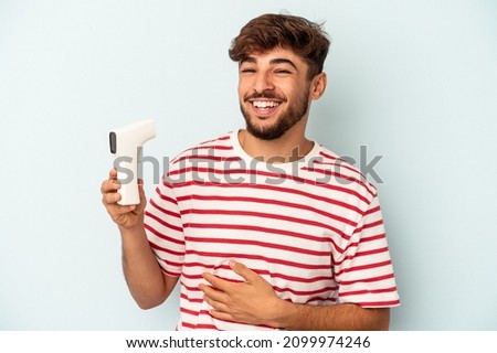 Young arab man holding thermometer isolated on blue background laughing and having fun.