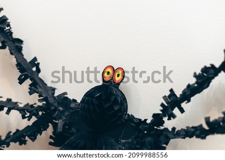 Big yellow eyes of black spider paper decor on white wall. Day of Dead. Halloween decoration.