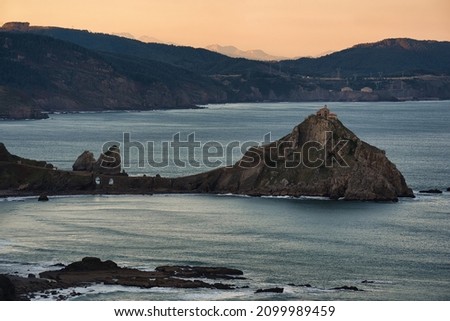 this is a photography of San Juan de Gaztelugatxe taken from Matxitxako at sunrise, the sun lights the background. There can be seen the shape of the rock, the upstairs and the little church