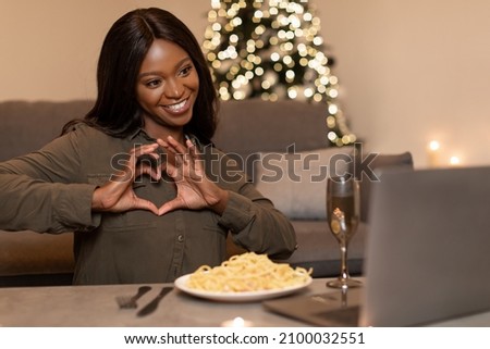 Black Millennial Lady Making Video Call Gesturing Heart Shape To Laptop Computer Celebrating Christmas Online Having Dinner Sitting At Home. Modern Distance Holiday And Communication