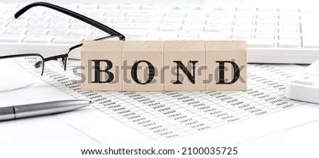 BOND written on wooden cube with keyboard , calculator, chart,glasses.Business