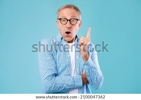 Wow, Eureka. Portrait of emotional mature man having great idea, finding inspiration or solution to problem. Excited amazed guy in glasses with open mouth pointing finger up on blue studio background