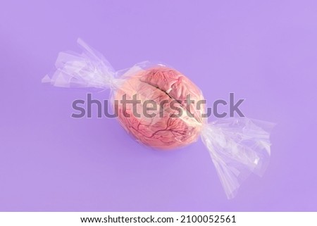 Candy made of human brain wrapped in cellophane on isolated pastel purple background. Halloween gifting trend. Minimal abstract science concept of memory, psychology or neurology. Creative card. Royalty-Free Stock Photo #2100052561