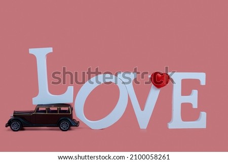 Retro car carries the word "Love" on a pink background. Valentine's Day.