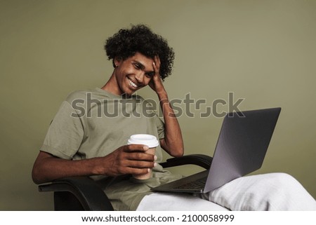 Young black man with piercing using laptop and drinking coffee isolated over green background