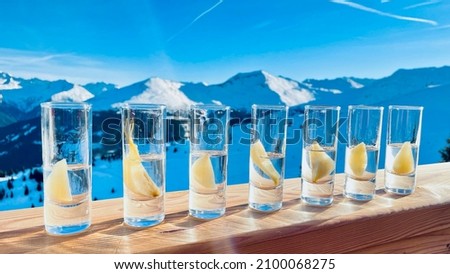 Shot glasses with williams pear schnapps on a banister in front of winter mountain background at ski slopes in the alps