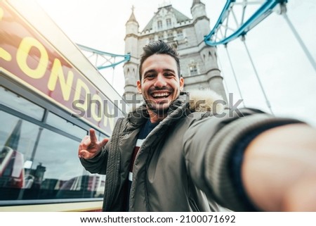 Smiling man taking selfie portrait during travel in London, England - Young tourist male taking memory pic with iconic england landmark - Happy people wandering around Europe concept Royalty-Free Stock Photo #2100071692