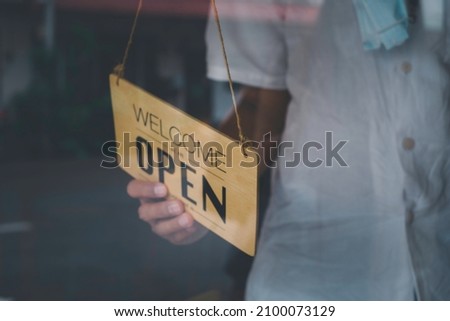 Blurred picture of hand turning signboard to open or reopen the store, restaurant after close lockdown quarantine. Store owner turning open sign broad through the door glass and ready to service. 