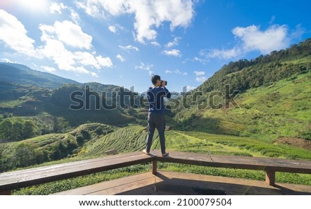 A tourist, a photographer holding a camera, travelling in holiday vacation with forest trees and green mountain hills. Nature landscape background, Thailand. People lifestyle.
