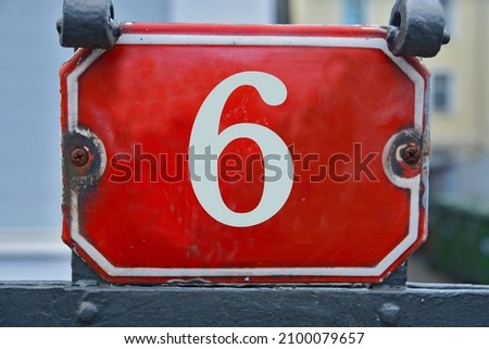 A red house number plaque, showing the number six (6)
