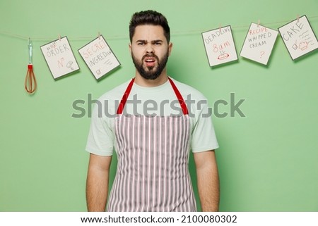 Young disappointed displeased dissatisfied sad outraged male chef confectioner baker man 20s wear striped apron isolated on plain pastel light green background studio portrait. Cooking food concept