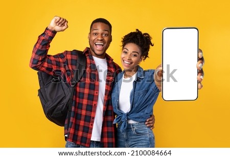Excited Casual Black Couple Holding Big Smartphone With Empty White Cell Screen In Hand, Shaking Fists, Planning Trip, Cheerful Young People Celebrating Win, Yellow Orange Studio Background, Mock Up