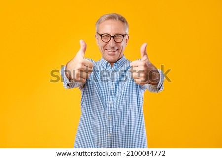 Best Choice, I Like It. Portrait of excited mature man in glasses showing thumbs up sign gesture with both hads, approving recommending. Happy senior male posing isolated on yellow orange studio wall Royalty-Free Stock Photo #2100084772