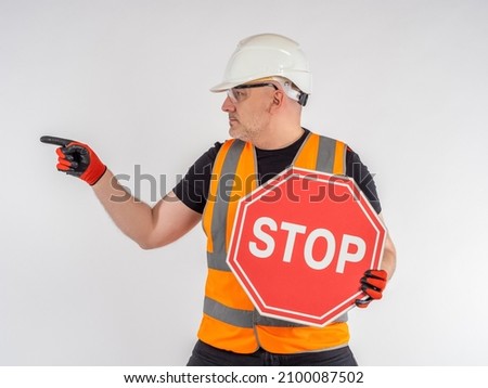 Stop road sign. Builder warns of danger. Worker indicates direction. Road hazard warning. Concept is prevention of accidents. Stop warning. Mature man in uniform of construction worker.