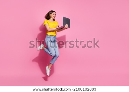 Photo of pretty shiny young woman wear yellow outfit jumping high typing modern device empty space smiling isolated pink color background