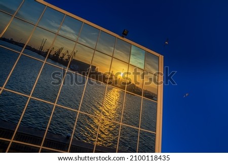 Modern glass building with reflected evening city and sunset sky in it. Sunset through window panels