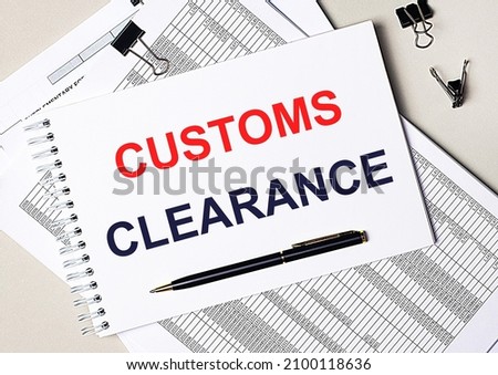 On the desktop there are documents, pen, black paper clips and a notebook with the text CUSTOMS CLEARANCE. Business concept